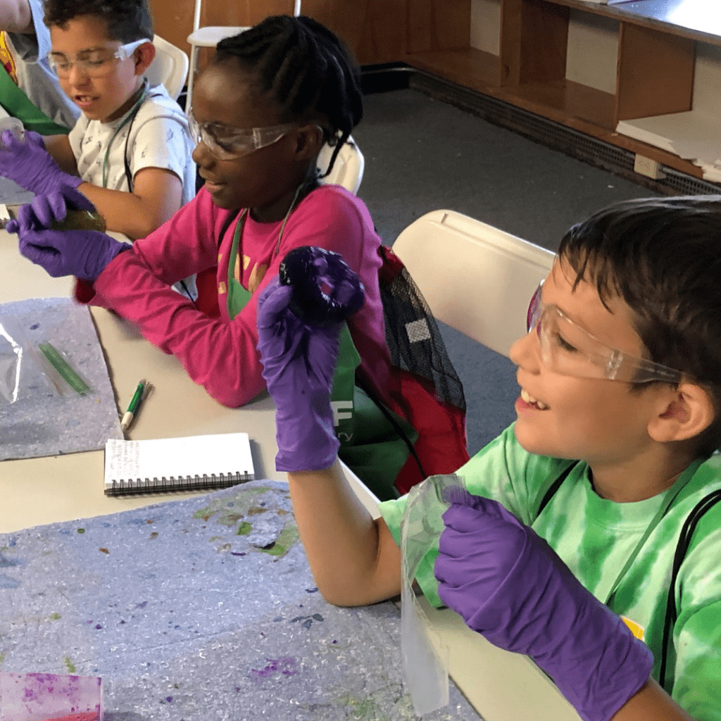 A group of children wearing purple gloves and green shirts.