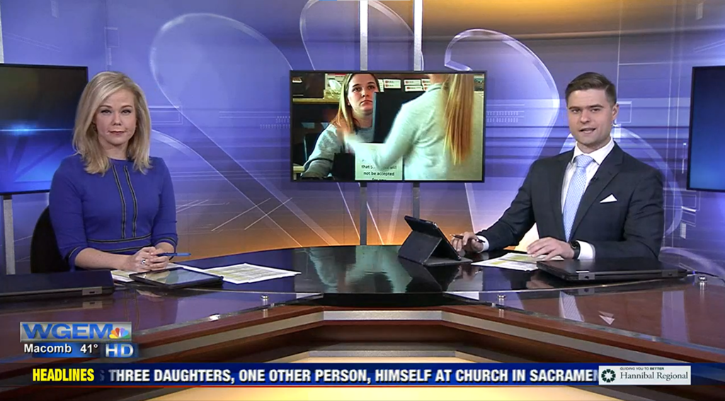 Two people are sitting at a table in front of a television.